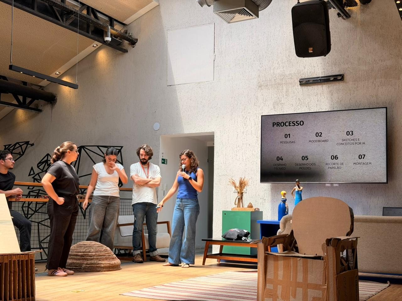 Equipe apresentando o processo de produção da Cadeira Bowl, com as etapas projetadas em um telão